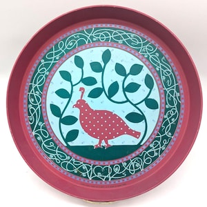 May include: A round, red metal tray with a decorative bird and leaf design. The bird is red with white polka dots, set against a light blue background. The tray's border features a green and white floral pattern, creating a vintage aesthetic.