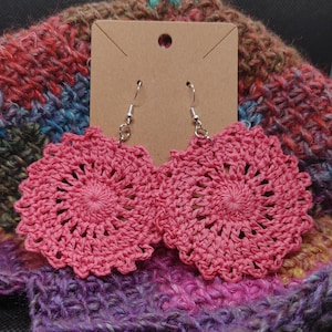 May include: A pair of pink crocheted earrings with silver hooks. The earrings are round and have a delicate, floral design.