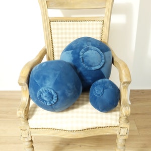 May include: Three blue velvet round pillows with a button detail on a light wood chair with a checkered fabric seat.