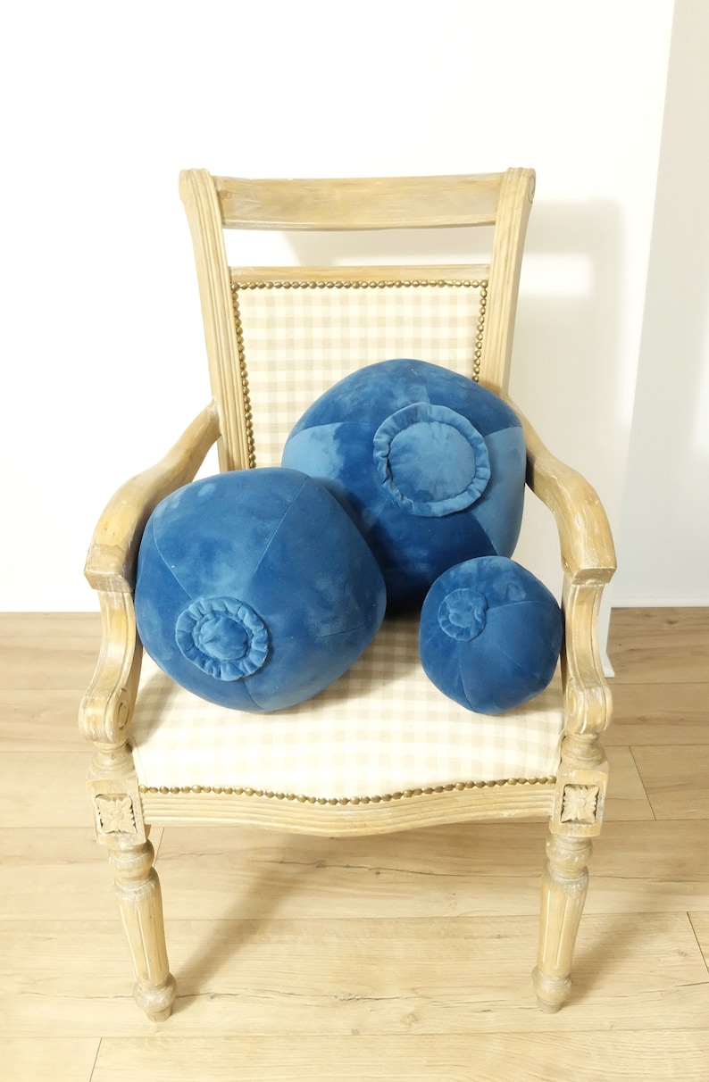 May include: Three blue velvet round pillows with a button detail on a light wood chair with a checkered fabric seat.