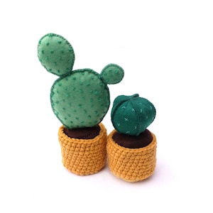 May include: Two felt cactus plants in crocheted pots. The larger cactus is green with a single arm and the smaller cactus is a round, dark green ball. Both pots are a mustard yellow colour.