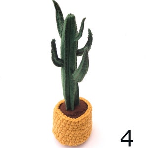 May include: A green felt cactus plant in a yellow crocheted pot. The cactus has multiple arms and is standing on a white surface. The number 4 is visible in the bottom right corner of the image.