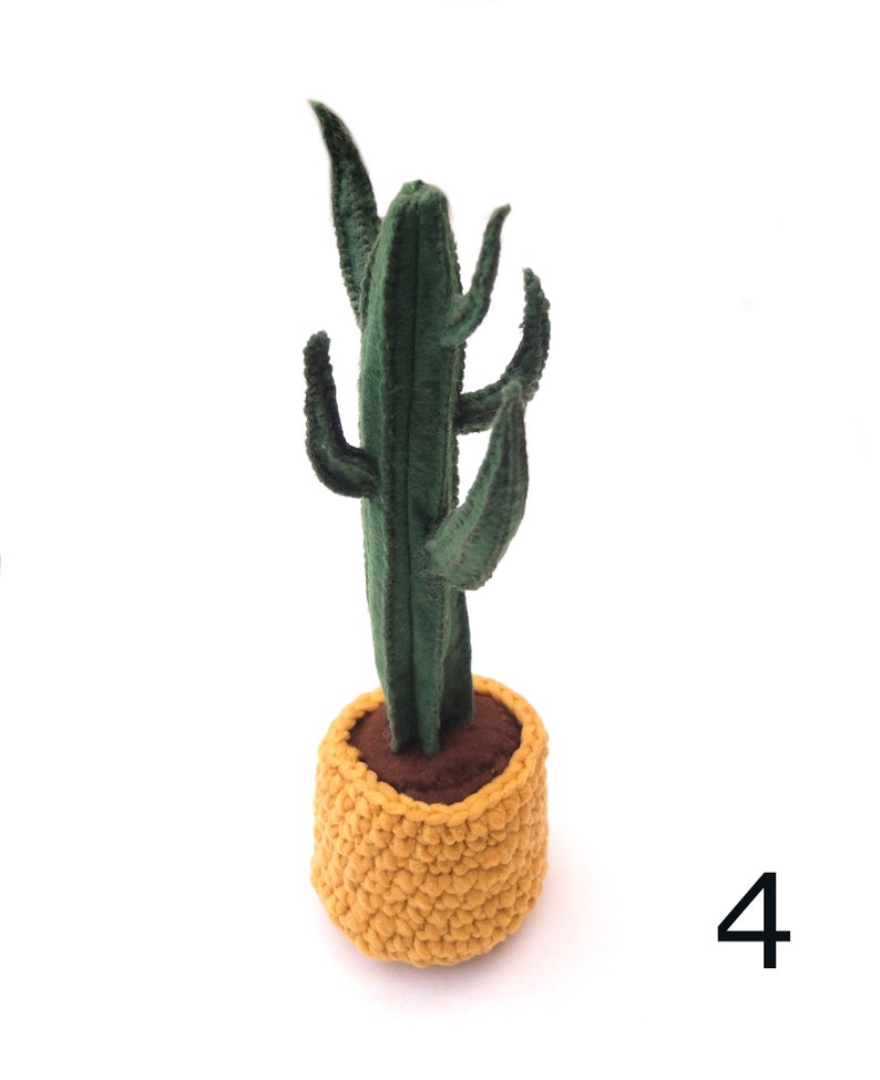 May include: A green felt cactus plant in a yellow crocheted pot. The cactus has multiple arms and is standing on a white surface. The number 4 is visible in the bottom right corner of the image.