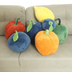 May include: A group of plush fruit-shaped pillows in various colors, including red, orange, yellow, green, and blue. The pillows are arranged on a light gray couch.