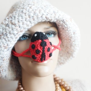 May include: A red and black ladybug nose mask with black eyes and a white crocheted hat.