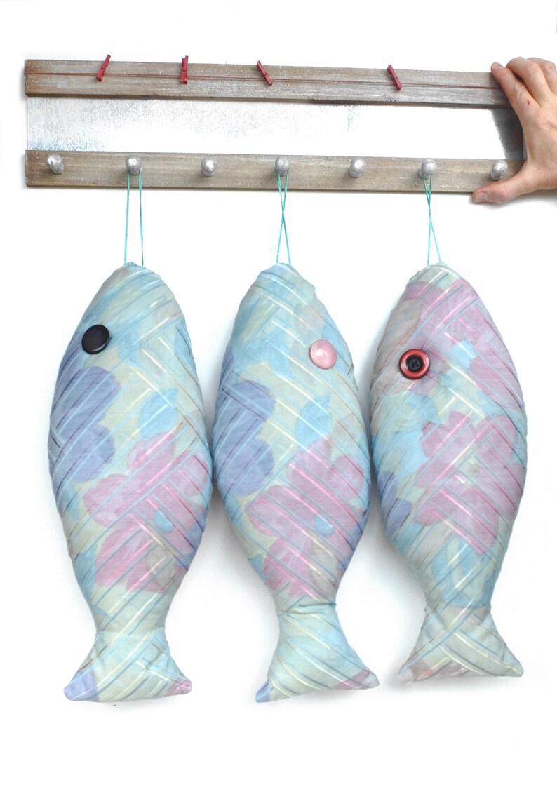 Peut inclure: Trois ornements en tissu en forme de poisson bleu et rose suspendus &agrave; un support en bois avec des crochets. Chaque poisson a un &oelig;il en bouton.