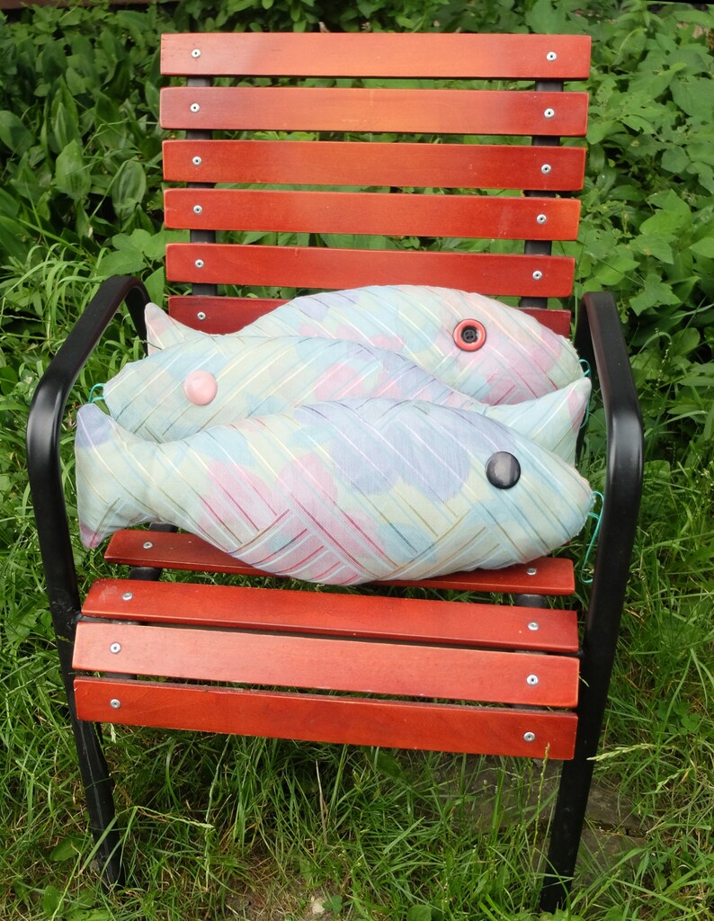 Peut inclure: Deux coussins en forme de poisson bleu et rose avec des yeux en boutons sur une chaise en bois rouge avec des pieds en m&eacute;tal noir.