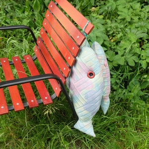 Peut inclure: Un banc en bois rouge &agrave; lattes avec un cadre en m&eacute;tal noir. Deux coussins en forme de poisson color&eacute;s sont suspendus au dos du banc.