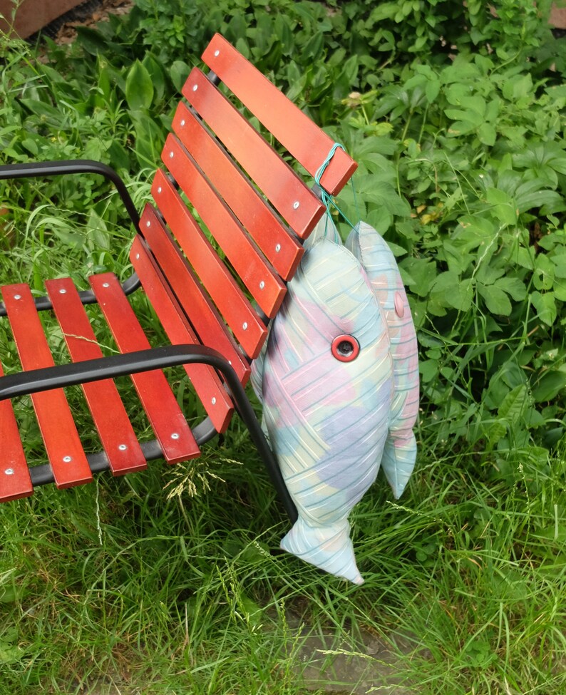 Peut inclure: Un banc en bois rouge &agrave; lattes avec un cadre en m&eacute;tal noir. Deux coussins en forme de poisson color&eacute;s sont suspendus au dos du banc.