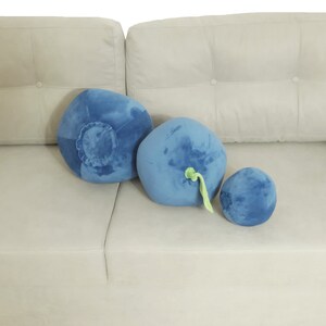 May include: Three plush blueberry pillows in different sizes on a light gray couch. The pillows are blue with green stems.