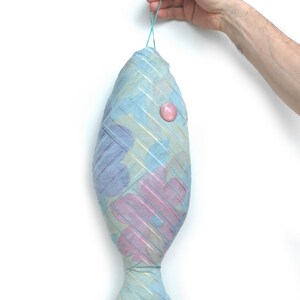 Peut inclure: Un poisson en tissu bleu et rose avec un bouton rose sur le c&ocirc;t&eacute;. Le poisson est suspendu &agrave; un &eacute;lastique bleu clair.