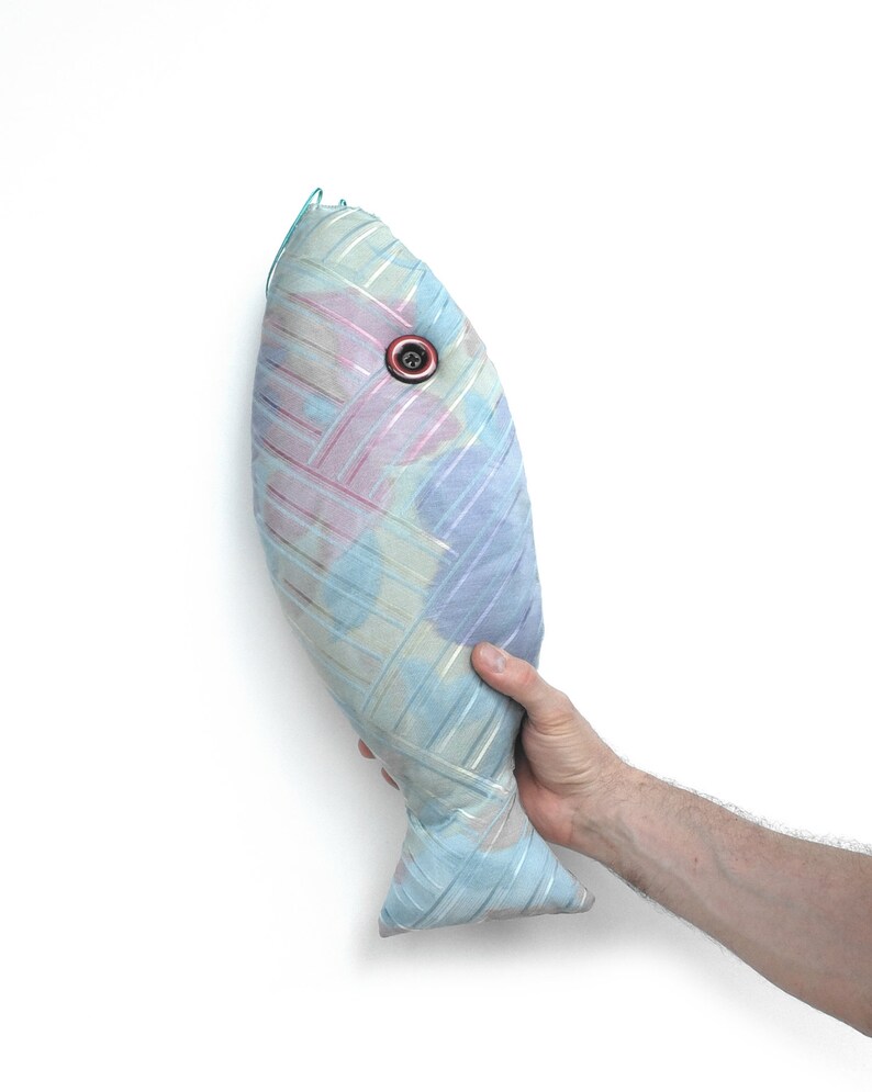 Peut inclure: Un coussin en forme de poisson bleu et rose avec un &oelig;il en bouton. Le coussin est fait d'un tissu doux et textur&eacute; et a un aspect l&eacute;g&egrave;rement d&eacute;lav&eacute;.