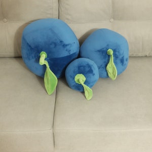 May include: Three plush blueberry pillows in different sizes, with green stems and leaves, on a light gray couch.
