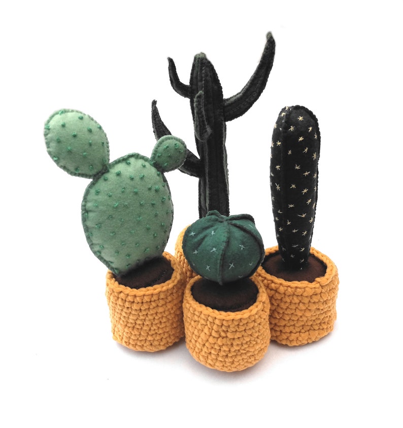 May include: Four potted cacti in various shapes and sizes. The cacti are made of felt and are in crocheted yellow pots. The cacti are green, black, and brown.