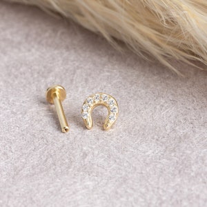 May include: A gold horseshoe shaped stud earring with clear cubic zirconia stones. The earring is shown with a straight post and a small ball on the end.