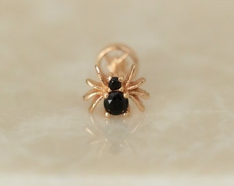 May include: Gold spider body piercing with black gemstones.