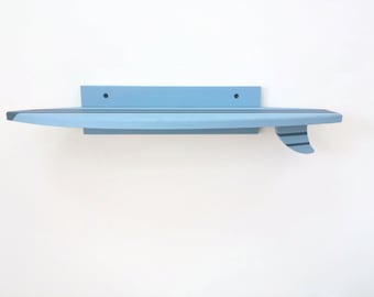 May include: A light blue surfboard shelf with black stripes and a fin. The shelf is mounted on a white wall.