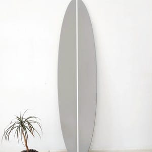 K&ouml;nnte beinhalten: Ein hohes, oval geformtes Surfbrett mit einer glatten, matten hellgrauen Oberfl&auml;che. Das Brett weist einen einzelnen, sauberen, vertikalen wei&szlig;en Streifen auf, der mittig von oben nach unten verl&auml;uft und ein symmetrisches Erscheinungsbild erzeugt.