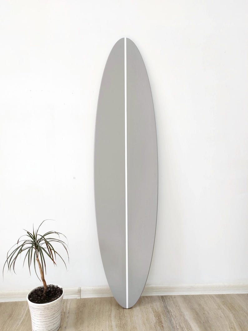 K&ouml;nnte beinhalten: Ein hohes, oval geformtes Surfbrett mit einer glatten, matten hellgrauen Oberfl&auml;che. Das Brett weist einen einzelnen, sauberen, vertikalen wei&szlig;en Streifen auf, der mittig von oben nach unten verl&auml;uft und ein symmetrisches Erscheinungsbild erzeugt.