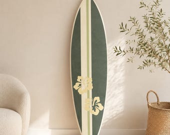 May include: A surfboard with a pointed tip and rounded tail, featuring a vertical design with dark green side panels, a central cream stripe, and a thin light green accent line. Two pale yellow hibiscus flower graphics are centred on the board.