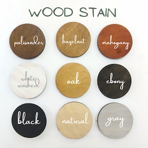 K&ouml;nnte beinhalten: Ein Raster aus neun runden Holzscheiben, die verschiedene Holzbeizfarben zeigen, beschriftet mit wei&szlig;em Schreibschrifttext: palisander, hazelnut, mahogany, white washed, oak, ebony, black, natural und gray. Der Titel WOOD STAIN steht oben.