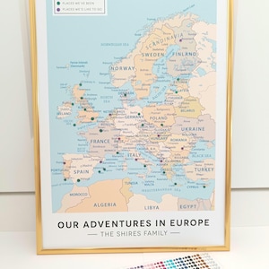 May include: A light blue map of Europe with gold push pins marking locations. The map is framed in gold and has the text "Our Adventures in Europe - The Shires Family" at the bottom.