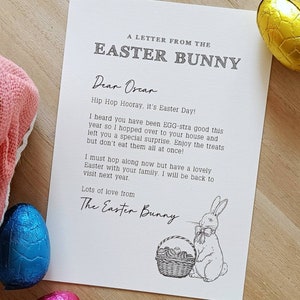 May include: A letter from the Easter Bunny to Oscar, with a drawing of a bunny and a basket of eggs. The letter is on a white paper with a wooden background. There are also chocolate eggs in the image.