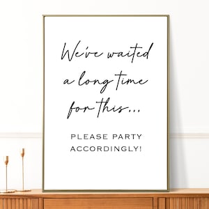 May include: White sign with black text that reads "We've waited a long time for this... Please party accordingly!"
