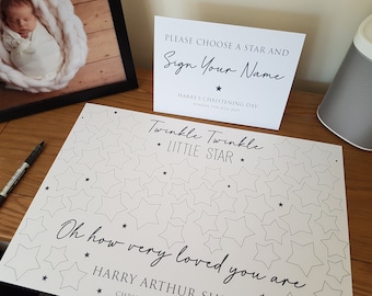 May include: A white sign with black text that reads "Please choose a star and sign your name."  The sign also includes the text "Harry's Christening Day, Sunday 7th July 2019".  A white sheet of paper with black stars and the text "Twinkle Twinkle Little Star" and "Oh how very loved you are" is on a wooden table.