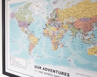May include: A framed world map with colorful countries and a blue ocean. The map is decorated with push pins in various colors. The text "OUR ADVENTURES - THE SHIRES FAMILY -" is printed at the bottom of the map.