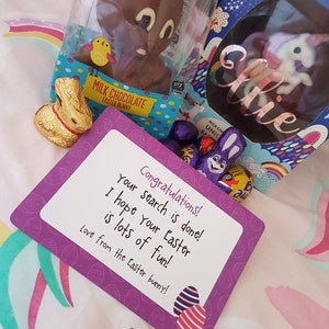 May include: A purple card with the text "Congratulations! Your search is done! I hope your Easter is lots of fun! Love from the Easter bunny!"  The card is decorated with images of Easter eggs. There is a chocolate Easter bunny, a chocolate egg with a unicorn inside, and a golden foil wrapped chocolate bunny.