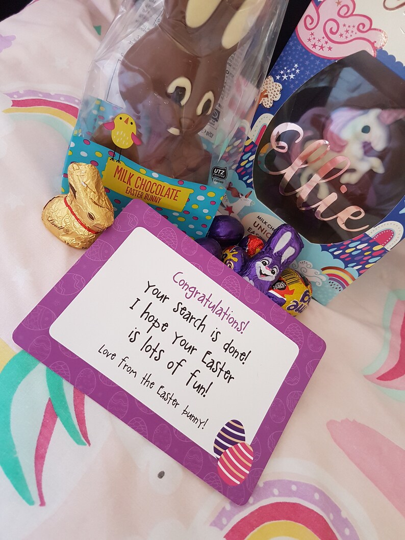 May include: A purple card with the text "Congratulations! Your search is done! I hope your Easter is lots of fun! Love from the Easter bunny!"  The card is decorated with images of Easter eggs. There is a chocolate Easter bunny, a chocolate egg with a unicorn inside, and a golden foil wrapped chocolate bunny.