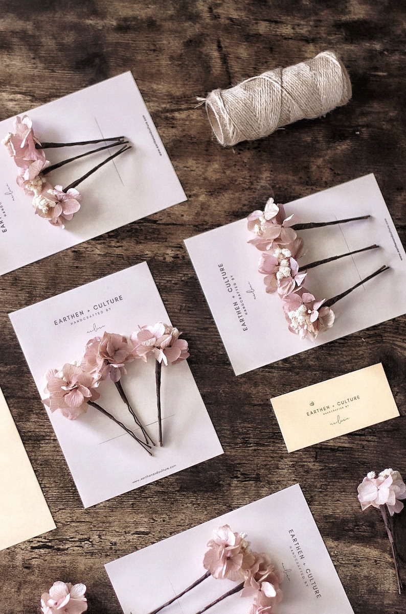 May include: Three sets of hair pins with dried pink flowers attached. Each set is displayed on a white card with the text "EARTHEN CULTURE HANDCRAFTED BY ubu" printed on it.