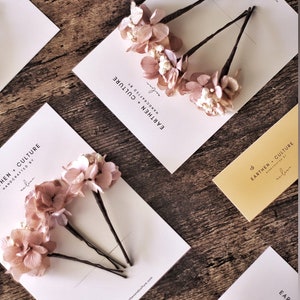 May include: Three sets of hair clips with dried pink flowers and a white card with the text "EARTHEN CULTURE HANDCRAFTED BY arlin" and the website address "www.earthasandculture.com".