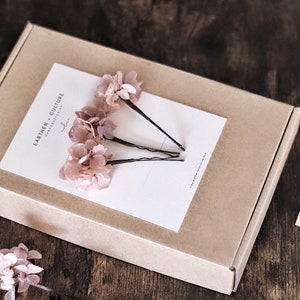 May include: Three pink flower hair clips in a brown box with a white card that says "Earthen Culture Handmade by..."