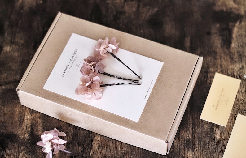 May include: Three pink flower hair clips in a brown box with a white card that says "Earthen Culture Handmade by..."