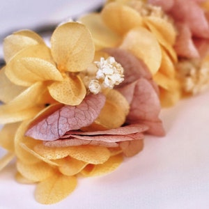 May include: A floral arrangement made of dried flowers in shades of yellow and pink. The flowers are arranged in a circular shape and have a delicate, rustic look.
