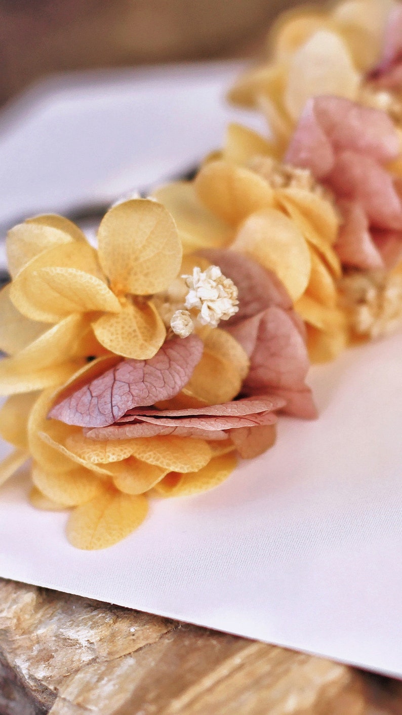 May include: A floral arrangement made of dried flowers in shades of yellow and pink. The flowers are arranged in a circular shape and have a delicate, rustic look.