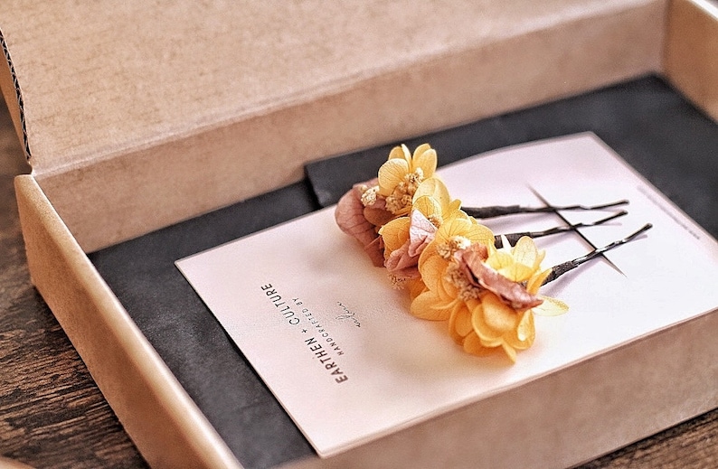 May include: Three yellow and brown dried flower hair clips in a small box with a pink card that says "Earthen Culture Handcrafted by"