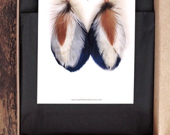 May include: A pair of feather earrings with blue, white, and brown feathers. The earrings are handcrafted by Earthen + Culture.