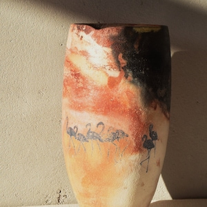 May include: A ceramic vase with a brown, orange, and white glaze. The vase has a black silhouette of a flock of birds on the side.