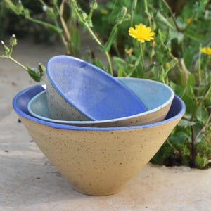 Peut inclure: Trois bols en céramique empilés, dans des tons de bleu et de beige. Le plus grand est beige avec un bord bleu, le milieu est bleu clair et le plus petit est bleu foncé. Les bols sont emboîtés.