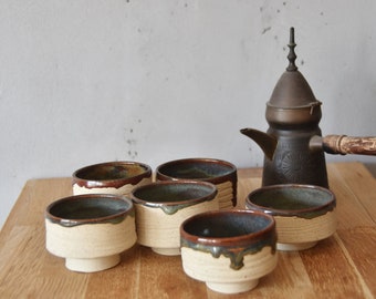 May include: Set of six brown and white ceramic teacups with a brown and brass teapot with a wooden handle.