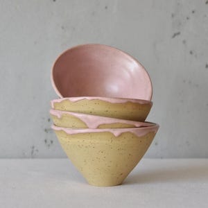 Könnte beinhalten: Ein Stapel von vier handgefertigten Keramikschalen. Die Schalen sind beige mit Sprenkeln, haben eine rosa Innenseite und eine rosa Glasur, die über den Rand tropft. Die Schalen sind gestapelt.