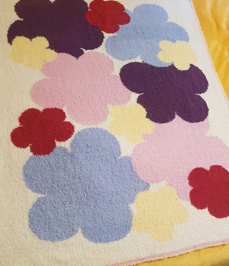 May include: A white rug with a colourful flower design. The flowers are in shades of pink, purple, yellow, red, and blue.