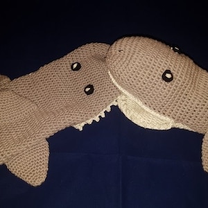 Könnte beinhalten: Zwei handgefertigte, gehäkelte Schals in Walform in hellbrauner Farbe. Jeder Schal hat schwarze Augendetails und einen weißen, gezackten Rand. Die Schals liegen auf einer dunkelblauen Oberfläche.