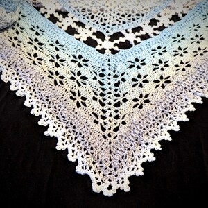 May include: A white crocheted shawl with a gradient of blue and purple hues. The shawl has a delicate lace pattern and a scalloped edge.
