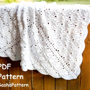May include: White crochet baby blanket with a scalloped edge and a textured pattern. The blanket is hanging on a wooden fence. The text "PDF Pattern SashaPattern" is visible at the bottom of the image.