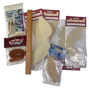 May include: Assortment of craft supplies including white and orange yarn, a ruler, and several packages of beige foam angel wings. The packages have the text "Homespun Traditions" printed on them.