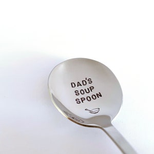 K&ouml;nnte beinhalten: Ein silberner Suppenl&ouml;ffel mit der Gravur "Dad's Soup Spoon". Unter dem Text ist ein kleines Schalen-Symbol graviert.